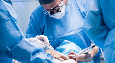 Three dentists in blue scrubs performing oral surgery