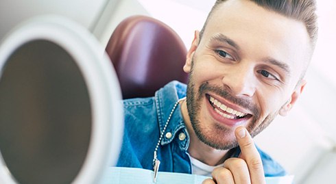 Man smiling at reflection in handheld mirror