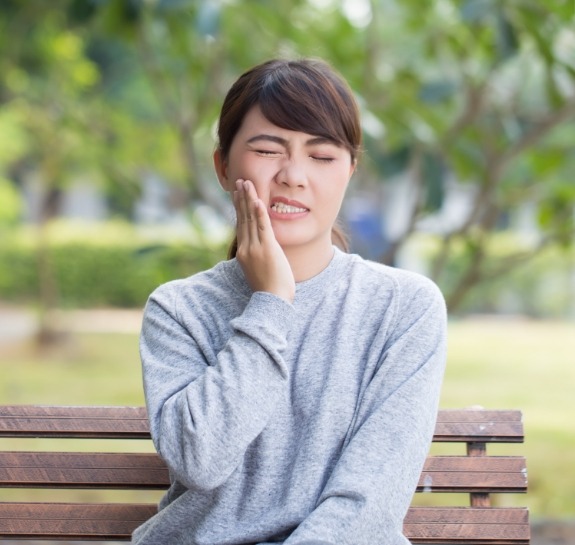 Woman on park bench holding her cheek in pain needing emergency dentist in Raleigh