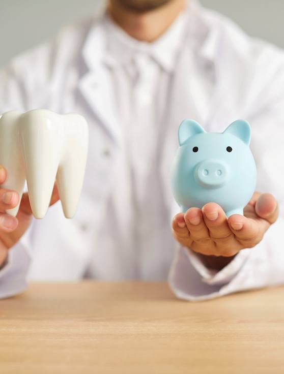 A dentist holding a model tooth and a piggy bank next to each other