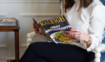 Person sitting in chair reading a magazine with cover that says Raleigh Best Restaurants