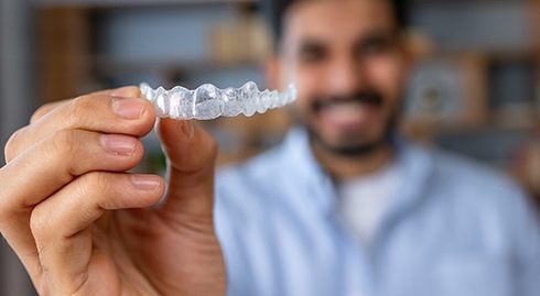 Smiling patient holding up clear aligner