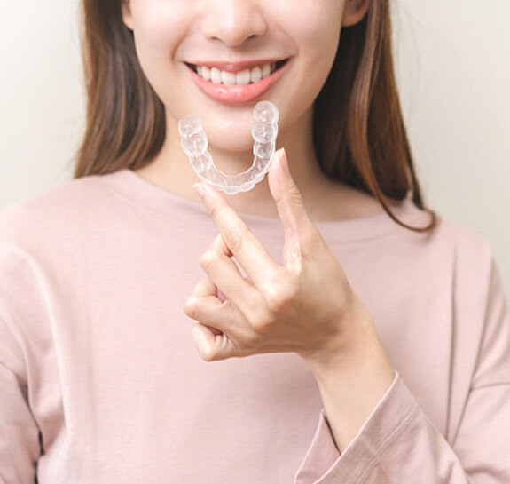 Woman smiling while holding clear aligner