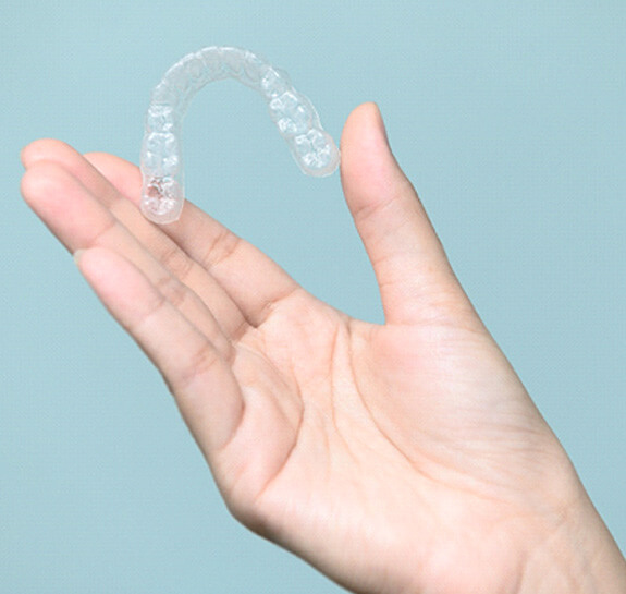 Patient holding clear aligner against blue background