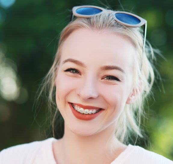 Young woman smiling outdoors with traditional braces in Raleigh