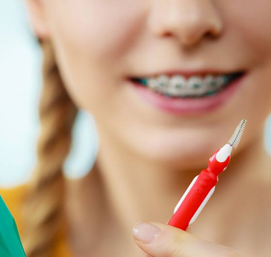 Closeup of standard and interproximal toothbrushes held to foreground by someone with braces